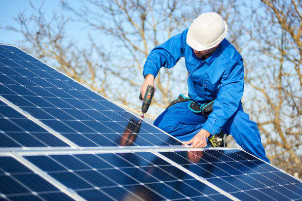 install 1 Male engineer in blue suit and protective helmet installing photovoltaic panel system using screwdriver. Professional electrician mounting solar module on roof. Alternative energy ecological concept.